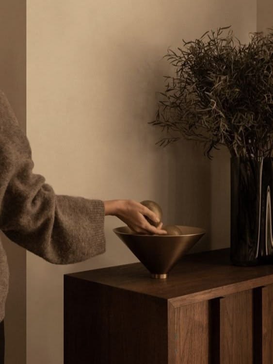 A hand placing a brass bowl on a dark wooden console — calm, considered and precise