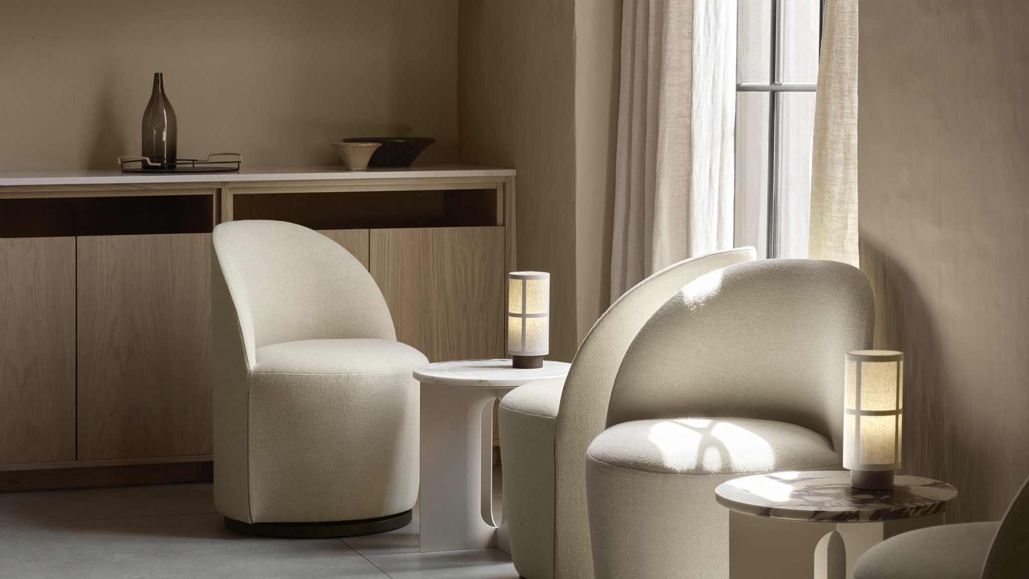 Cream lounge chairs beside a window with sheer curtains — calm, refined residential atmosphere